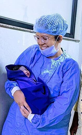 Dr. Anjani Dixit in surgical scrubs holding a newborn moments after delivery