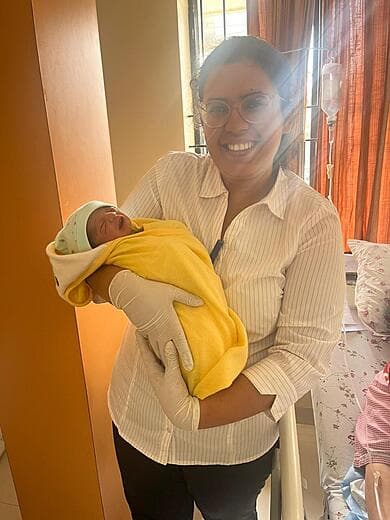 Dr. Anjani Dixit holding a newborn in a yellow blanket beside the mother’s bed